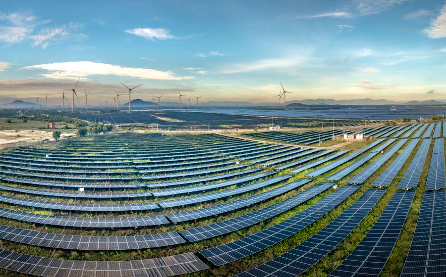 Expansive solar farm with wind turbines on the horizon