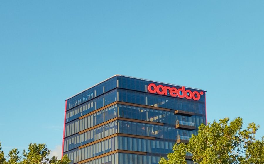 Modern glass office building surrounded by trees under a clear sky